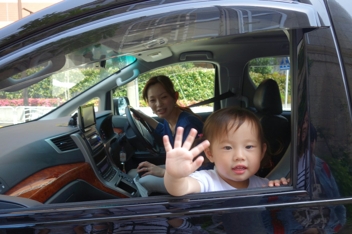Un enfant fait signe par la fenêtre de la voiture, sa mère au volant